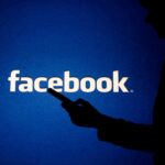 Facebook WHISTLEBLOWER Issues Dire Warning silhouette holding a smartphone in front of Facebook logo