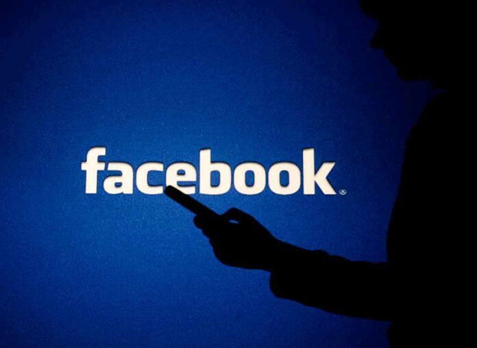 silhouette holding a smartphone in front of Facebook logo