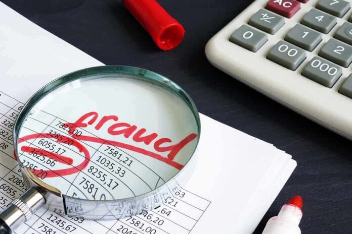 shutterstock_1165019509 Magnifying glass over financial spreadsheet with red marker and calculator