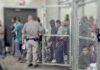 People standing inside chain-link holding area with an officer nearby