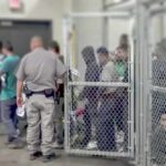 3.1 Million Visa Overstay Leads People standing inside chain-link holding area with an officer nearby