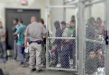 People standing inside chain-link holding area with an officer nearby