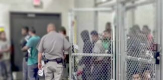 People standing inside chain-link holding area with an officer nearby
