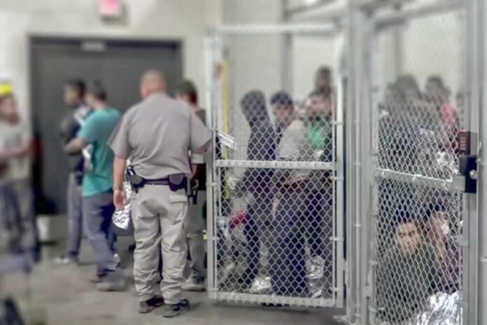 People standing inside chain-link holding area with an officer nearby