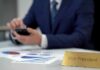 Business executive using smartphone at desk with charts and nameplate