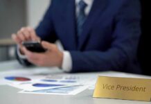 Business executive using smartphone at desk with charts and nameplate