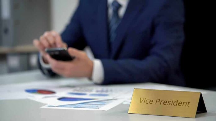 shutterstock_1312811357 Business executive using smartphone at desk with charts and nameplate