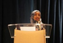 Ilhan Omar’s Legal NIGHTMARE Just Got Worse Woman in hijab speaking at a podium