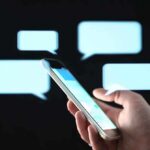 Hand holding smartphone with chat bubbles on dark background