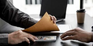 Hands exchanging cash in an envelope at a desk