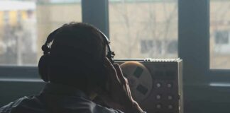 Person wearing headphones listening to a reel-to-reel tape recorder