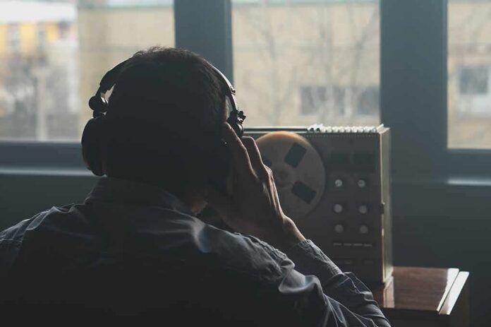 shutterstock_2164991019 Person wearing headphones listening to a reel-to-reel tape recorder