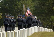 VA Funeral Benefits Leave Families With GAPS Military honor guard marches through a cemetery with flags