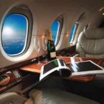 DHS Paid MILLIONS More for Luxury Jets private jet cabin with leather seat, champagne and magazine on table