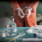Medical vials and IV lines on a table with a handcuffed person in the background