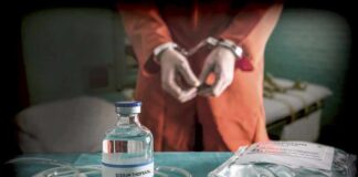 Medical vials and IV lines on a table with a handcuffed person in the background